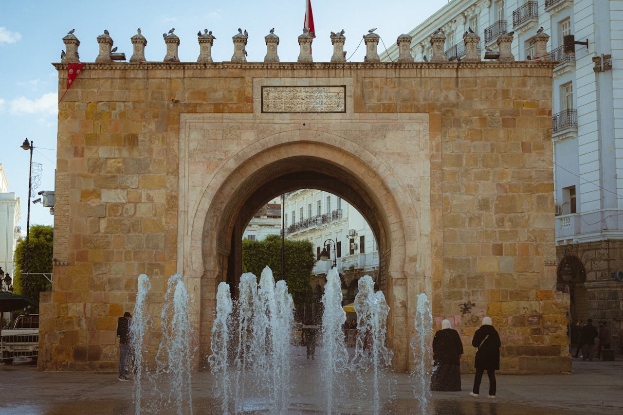 gallery-2 Bab el Bhar Gate in Tunis with a lively fountain scene and people in the foreground.