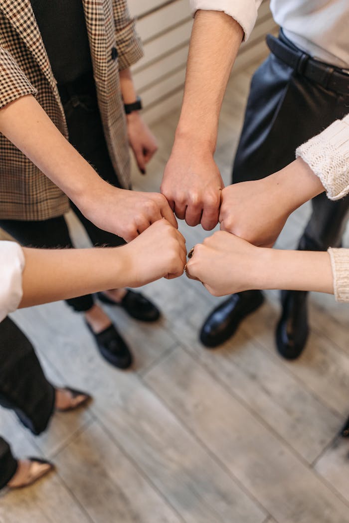 why-choose-us A close-up of five people fist bumping, symbolizing teamwork and unity indoors.