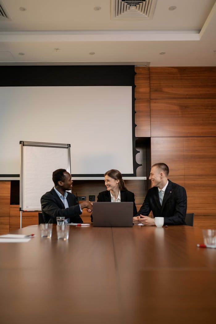 hero-img-02 Three professionals engaging in a handshake during a business meeting in a modern office setting.